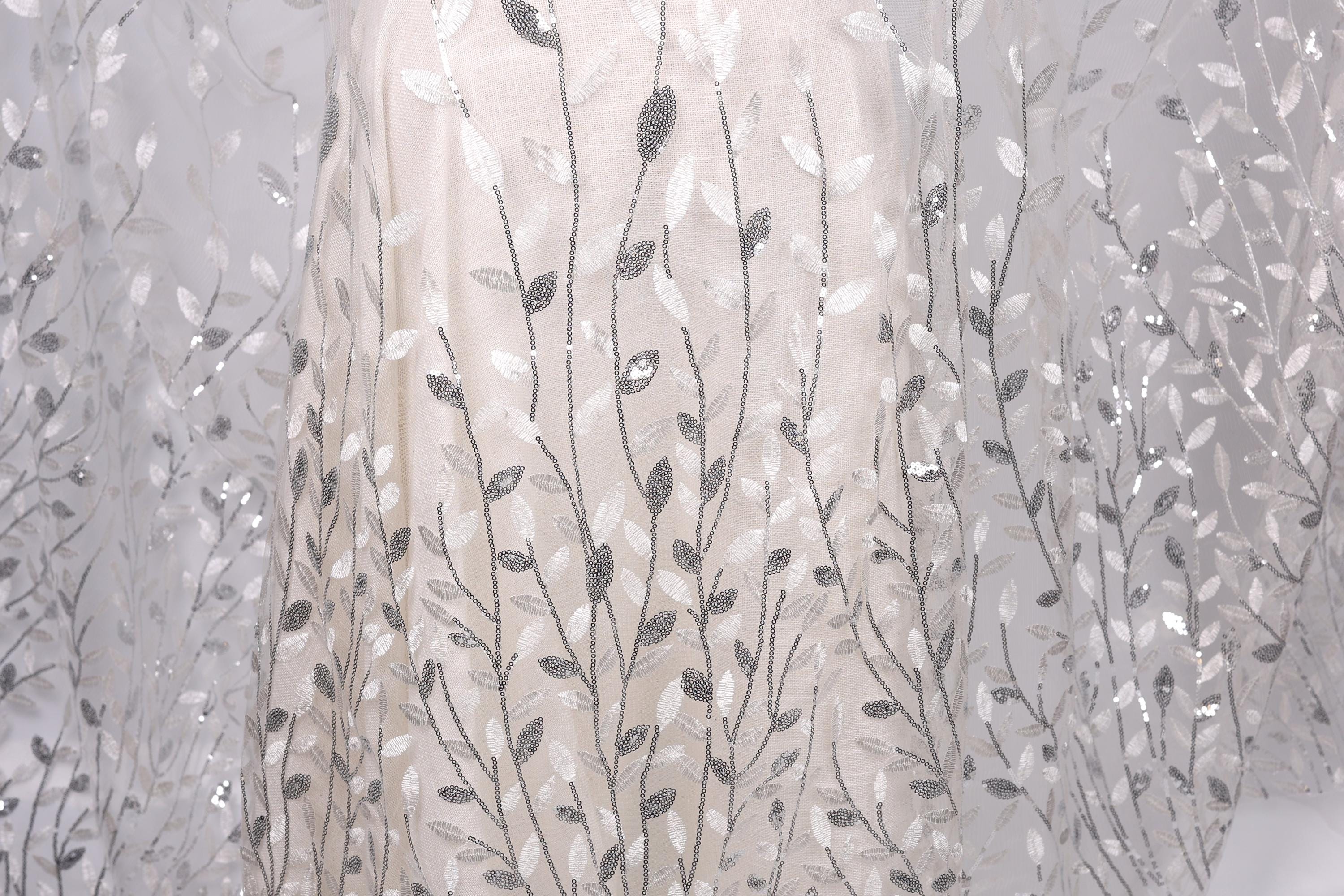 a close-up view of a delicate, white dress with a pattern of silver and white leaves or branches. The dress appears to be made of a sheer fabric, giving it a delicate and elegant appearance.