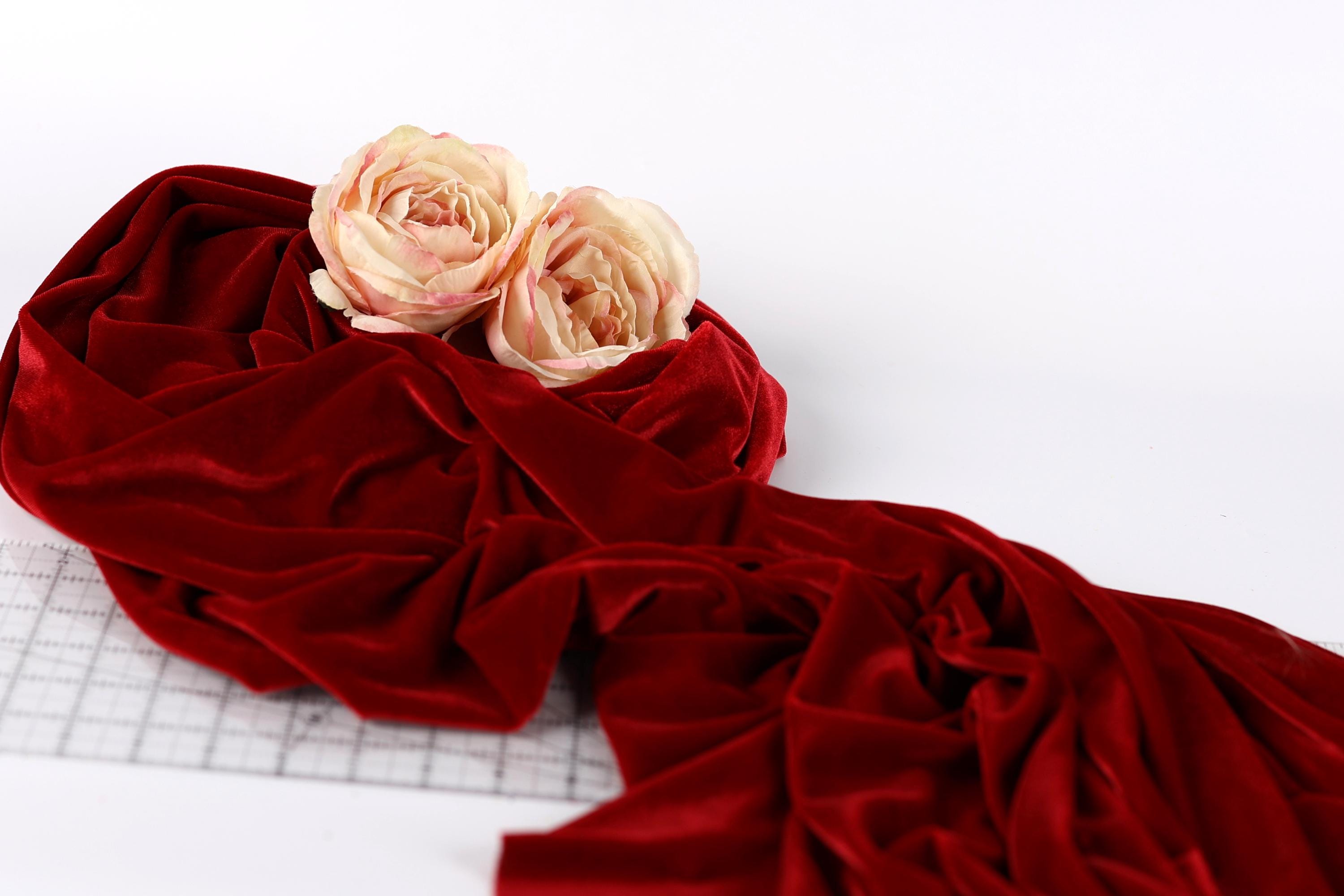 two pink roses resting on a crumpled red velvet fabric.