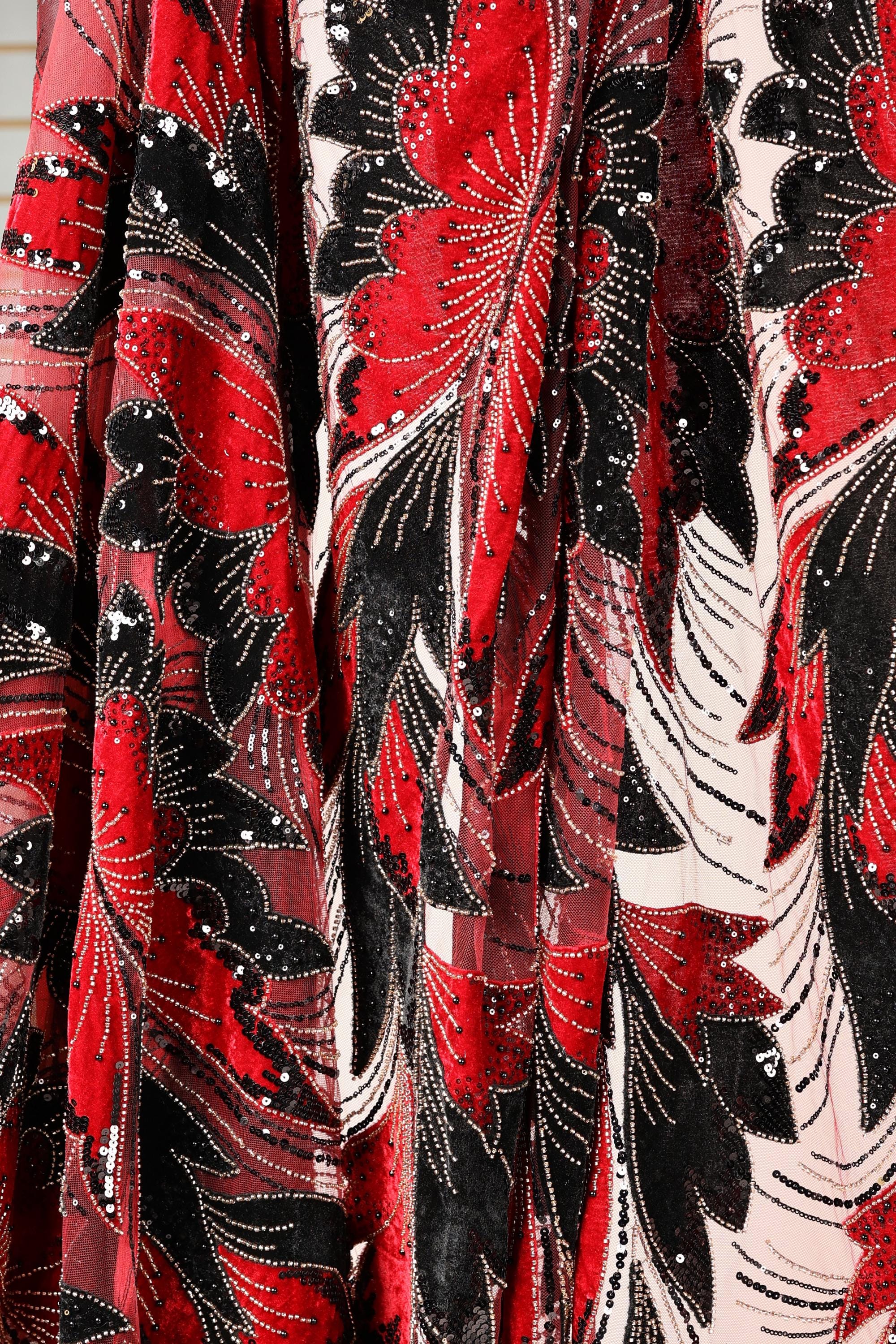 a close-up view of a fabric with a striking red and black floral pattern. The fabric appears to be made of a sheer material, with a mix of red, black, and white colors. The pattern is intricate and detailed, showcasing the craftsmanship of the fabric.