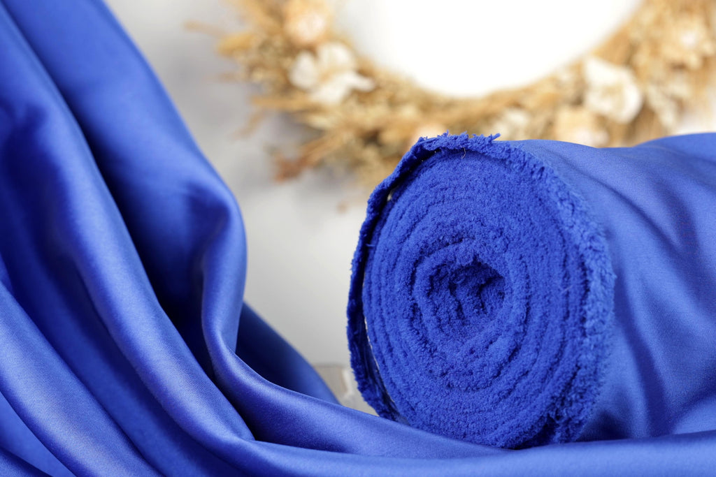 A close-up view of a blue fabric roll, with a blurred background featuring a wreath made of dried flowers.