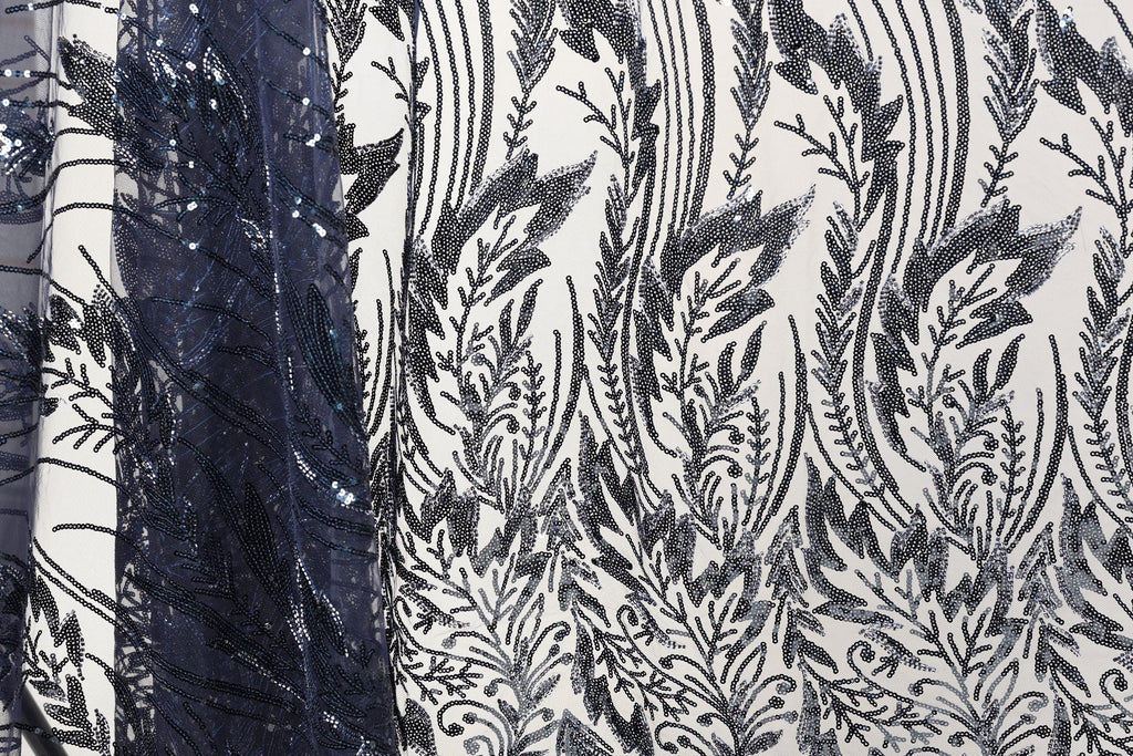 a close-up view of a fabric with a black and white floral pattern. The fabric appears to be made of a material with sequins or beads, adding a decorative element to the design. The pattern is intricate and detailed, showcasing the craftsmanship and artistry involved in creating the fabric.