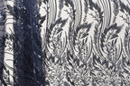 a close-up view of a fabric with a black and white floral pattern. The fabric appears to be made of a material with sequins or beads, adding a decorative element to the design. The pattern is intricate and detailed, showcasing the craftsmanship and artistry involved in creating the fabric.