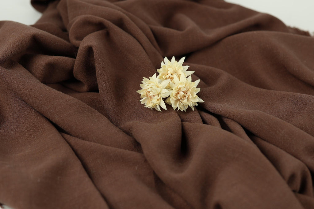 A close-up image of a delicate white flower resting on a brown fabric, creating a serene and elegant composition.