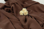 A close-up image of a delicate white flower resting on a brown fabric, creating a serene and elegant composition.