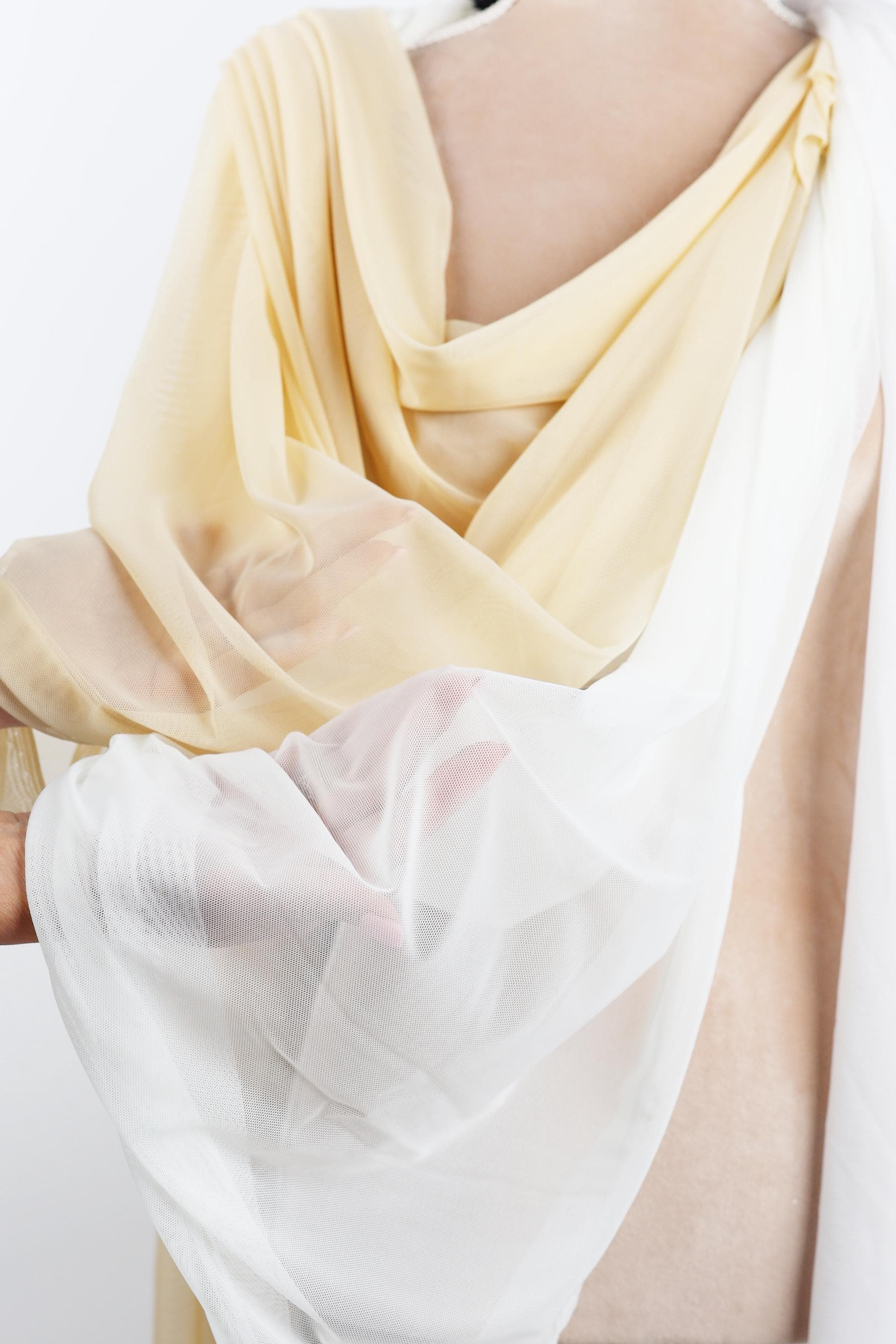 A close-up view of a person's torso wearing a yellow and white draped garment, with a white fabric draped over the person's shoulder.