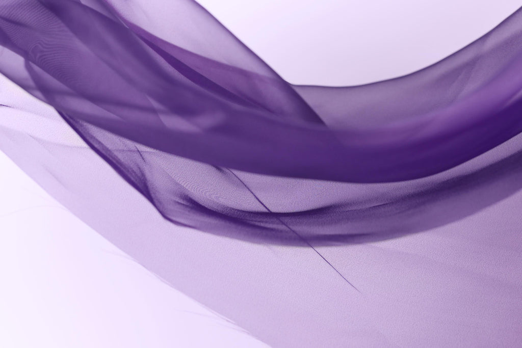 a close-up view of a flowing, purple fabric, with a soft and delicate texture. The fabric appears to be made of a sheer material, giving it a light and airy appearance. The image does not contain any discernible objects or actions, and the focus is solely on the fabric and its flowing nature.