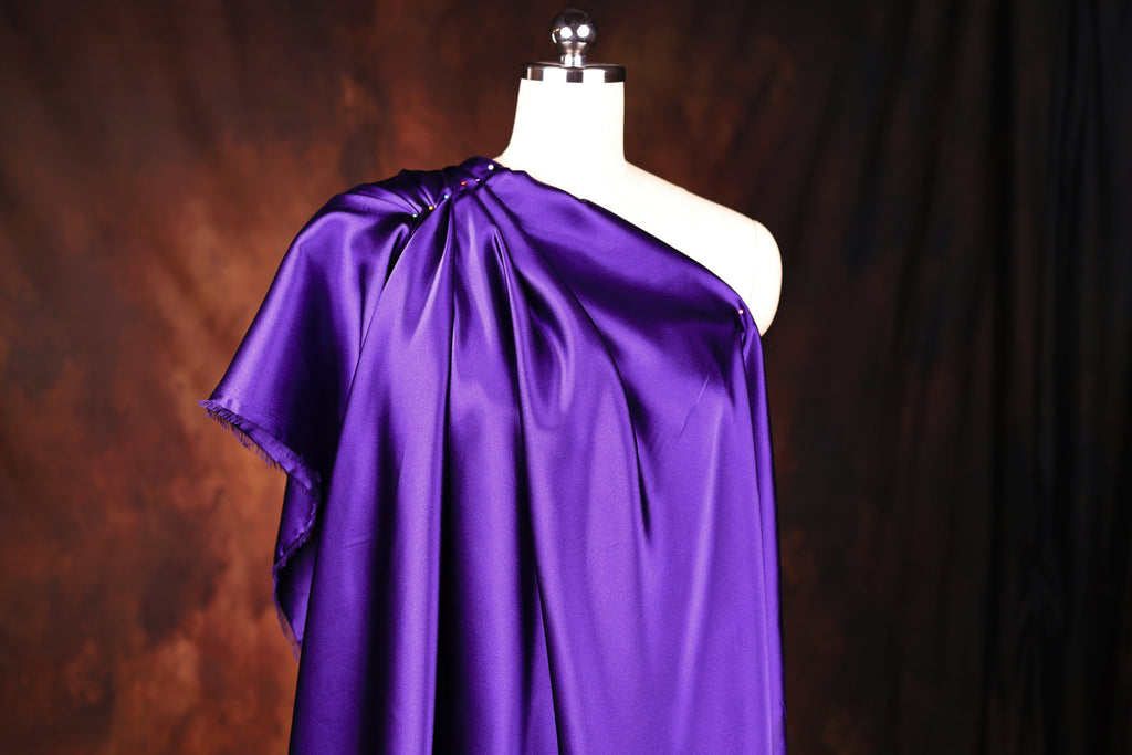 A mannequin wearing a purple one-shoulder dress against a dark background.