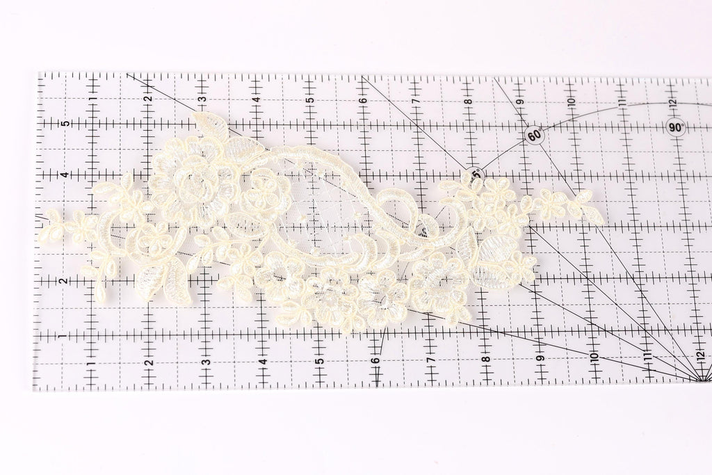 a piece of white lace with intricate floral patterns placed on a transparent ruler.