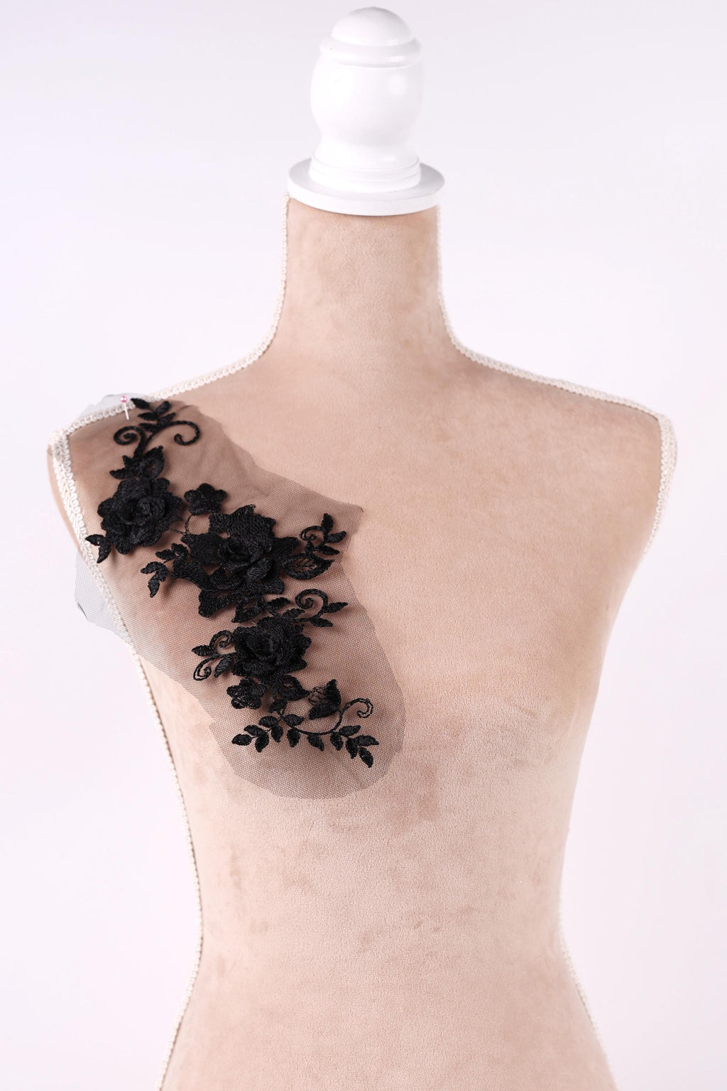 A mannequin with a beige body and a black lace overlay on its shoulder.
