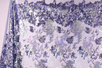 a fabric with a purple and white pattern, with a mix of small and large sequins or beads scattered across the fabric. The pattern appears to be a blend of different shades of purple and white, creating a visually striking and intricate design.