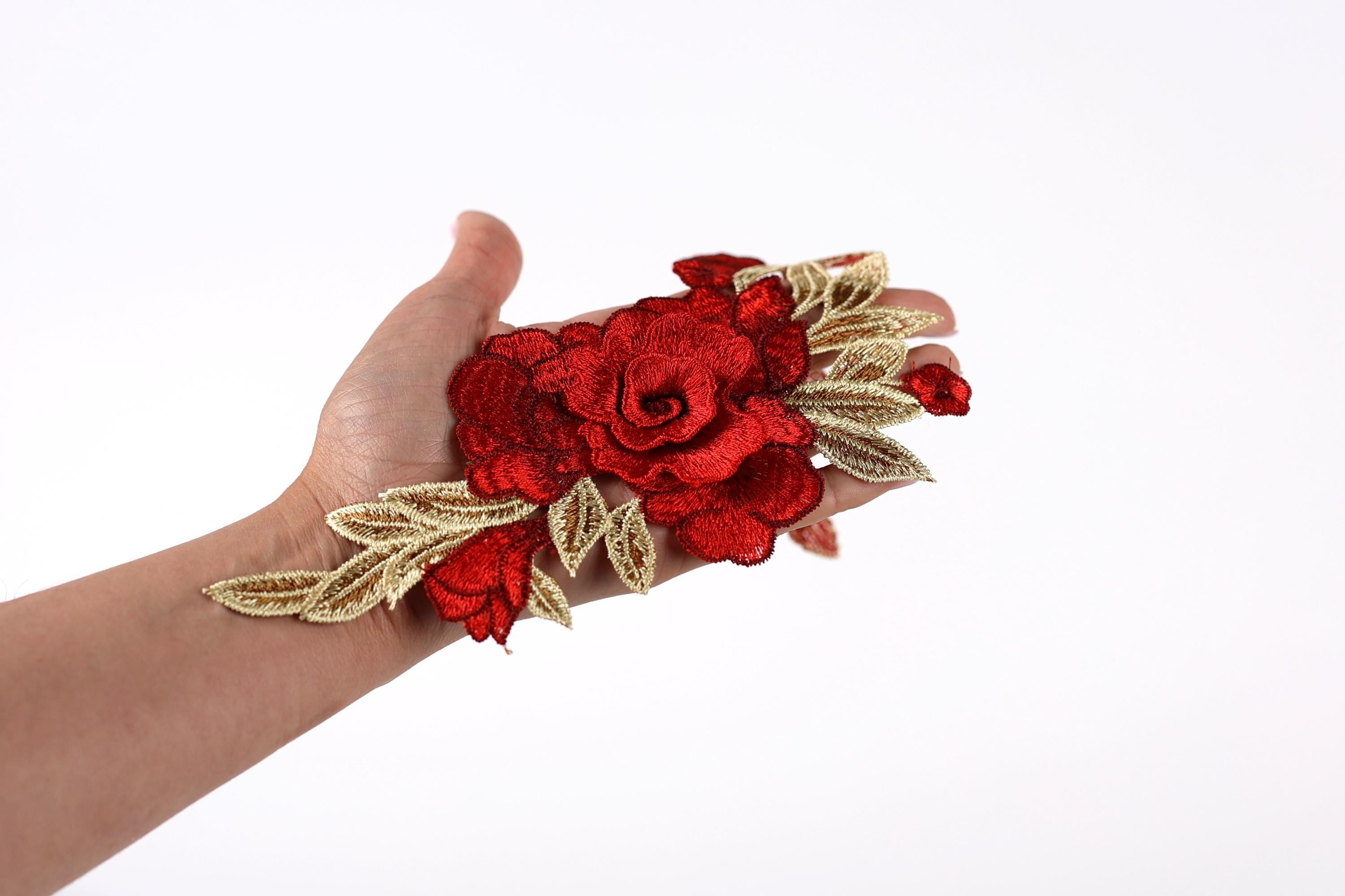 A hand holding a red flower with gold leaves against a white background.
