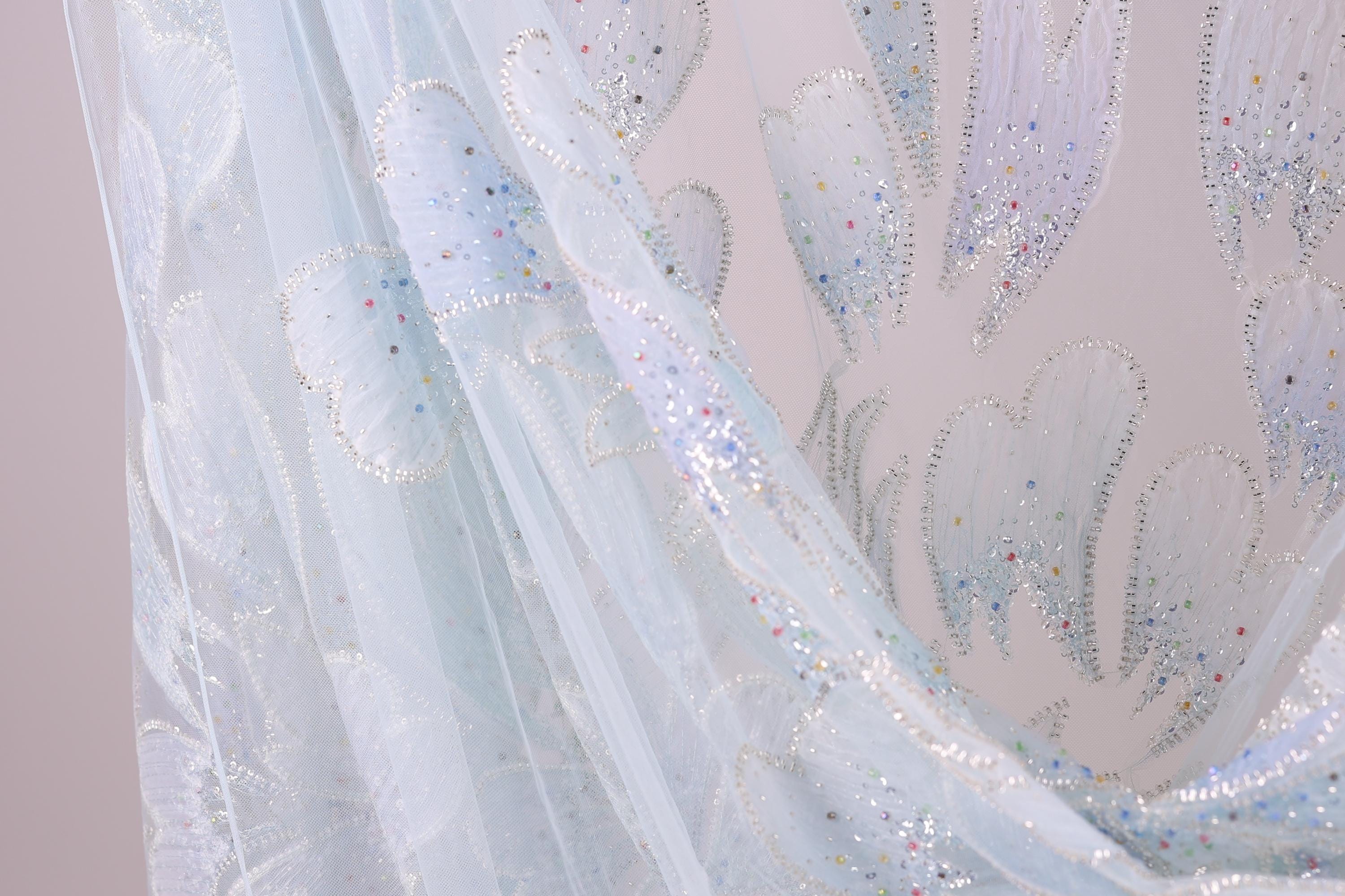 a close-up view of a delicate, light blue fabric with a pattern of small, colorful dots or sequins. The fabric appears to be made of sheer material, giving it a soft and delicate appearance.
