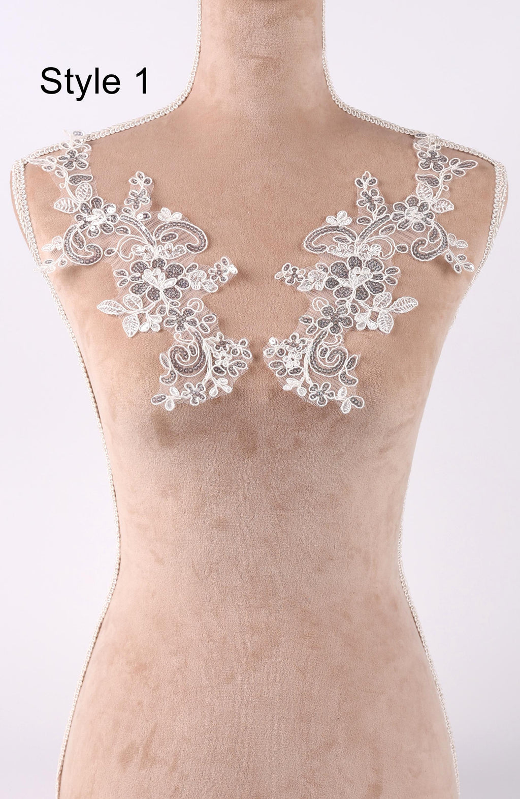A mannequin wearing a beige dress with delicate white lace floral embroidery on the shoulders.