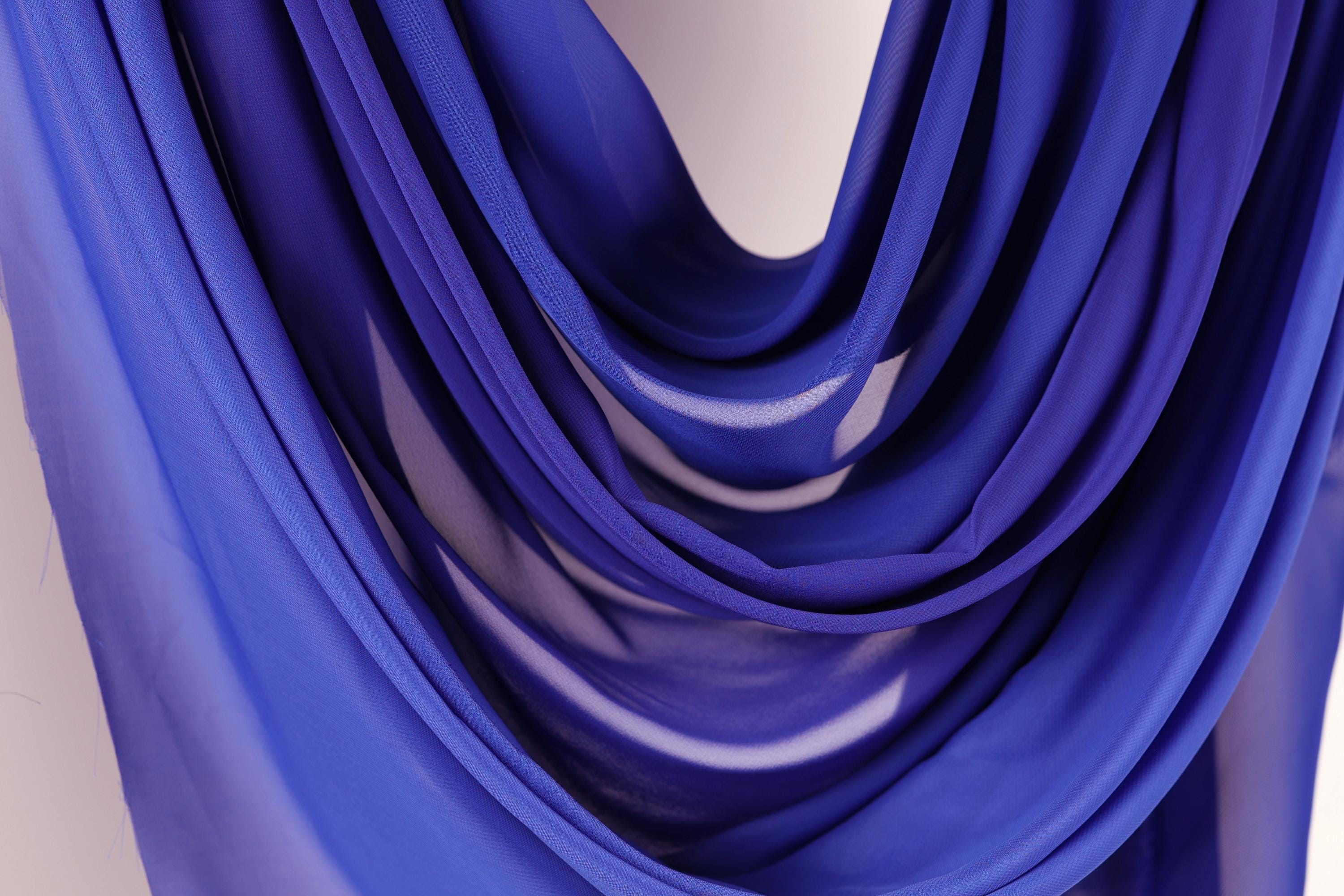 a close-up view of a blue fabric, possibly a chiffon or sheer material, with a soft, flowing texture. The fabric appears to be draped or draped over a surface, creating a sense of movement and depth.