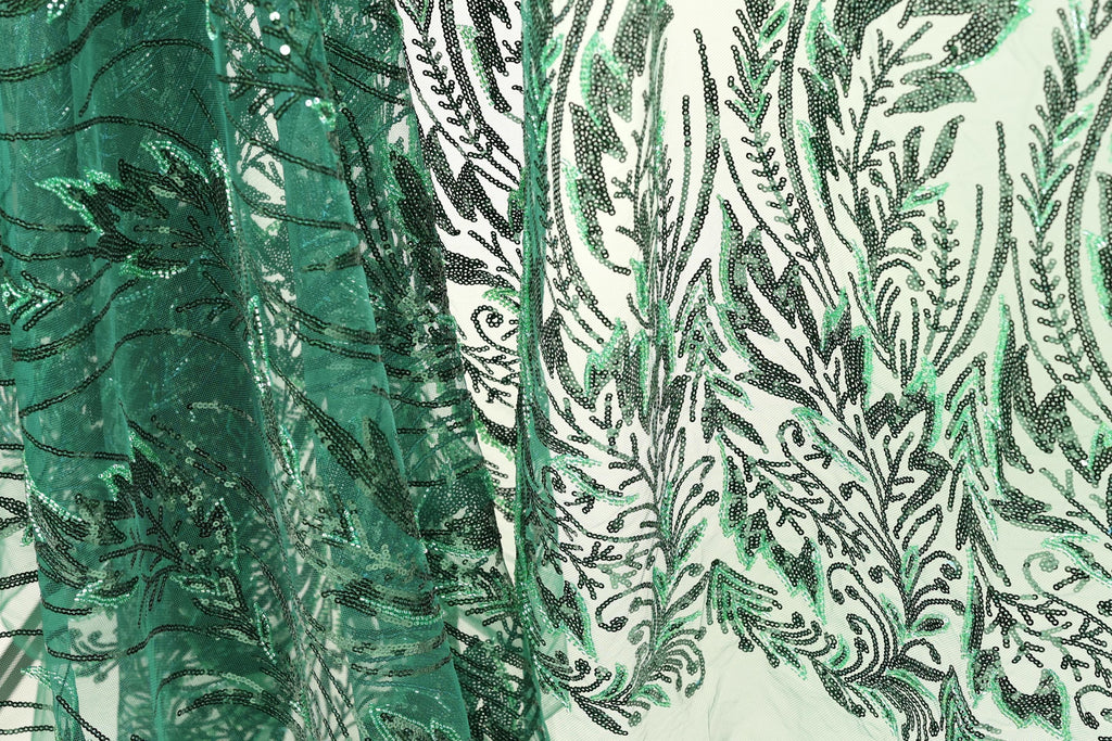 a close-up view of a fabric with a green and black floral pattern. The fabric appears to be made of a material with a textured surface, possibly lace or a similar type of material. The pattern consists of various shapes and designs, including leaves, flowers, and other decorative elements, creating a visually striking and intricate design.