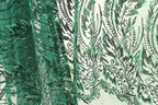 a close-up view of a fabric with a green and black floral pattern. The fabric appears to be made of a material with a textured surface, possibly lace or a similar type of material. The pattern consists of various shapes and designs, including leaves, flowers, and other decorative elements, creating a visually striking and intricate design.