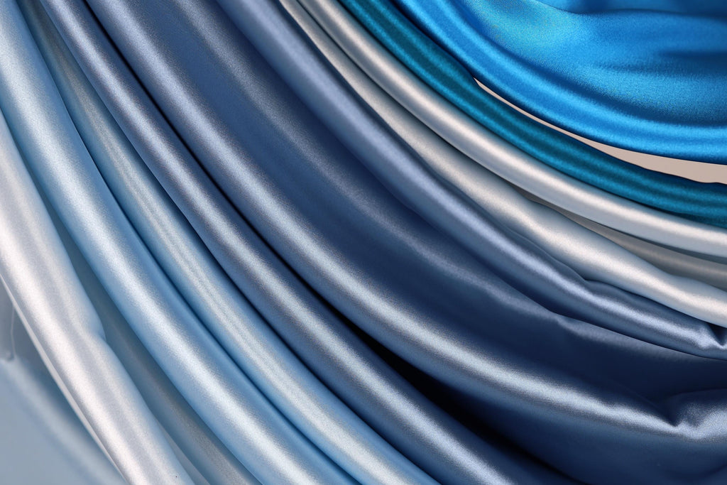 a close-up view of a collection of blue and silver satin fabric, with the fabric appearing to be folded or draped in a cascading manner.