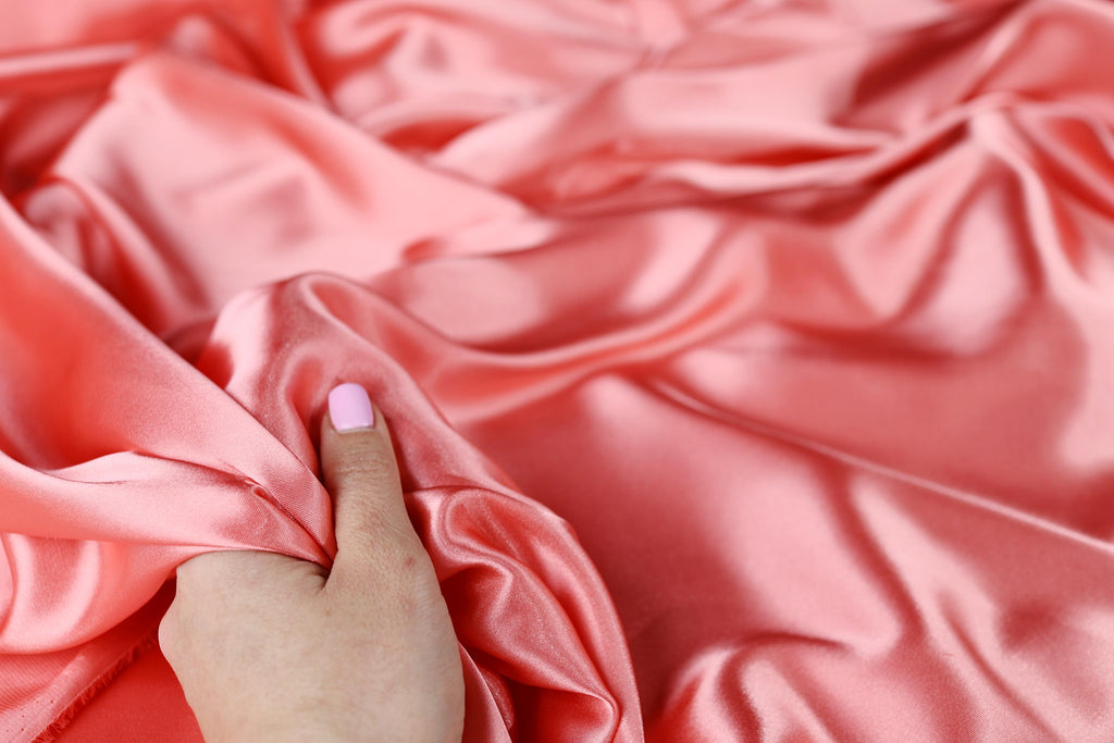 a person&#39;s hand on a pink satin fabric