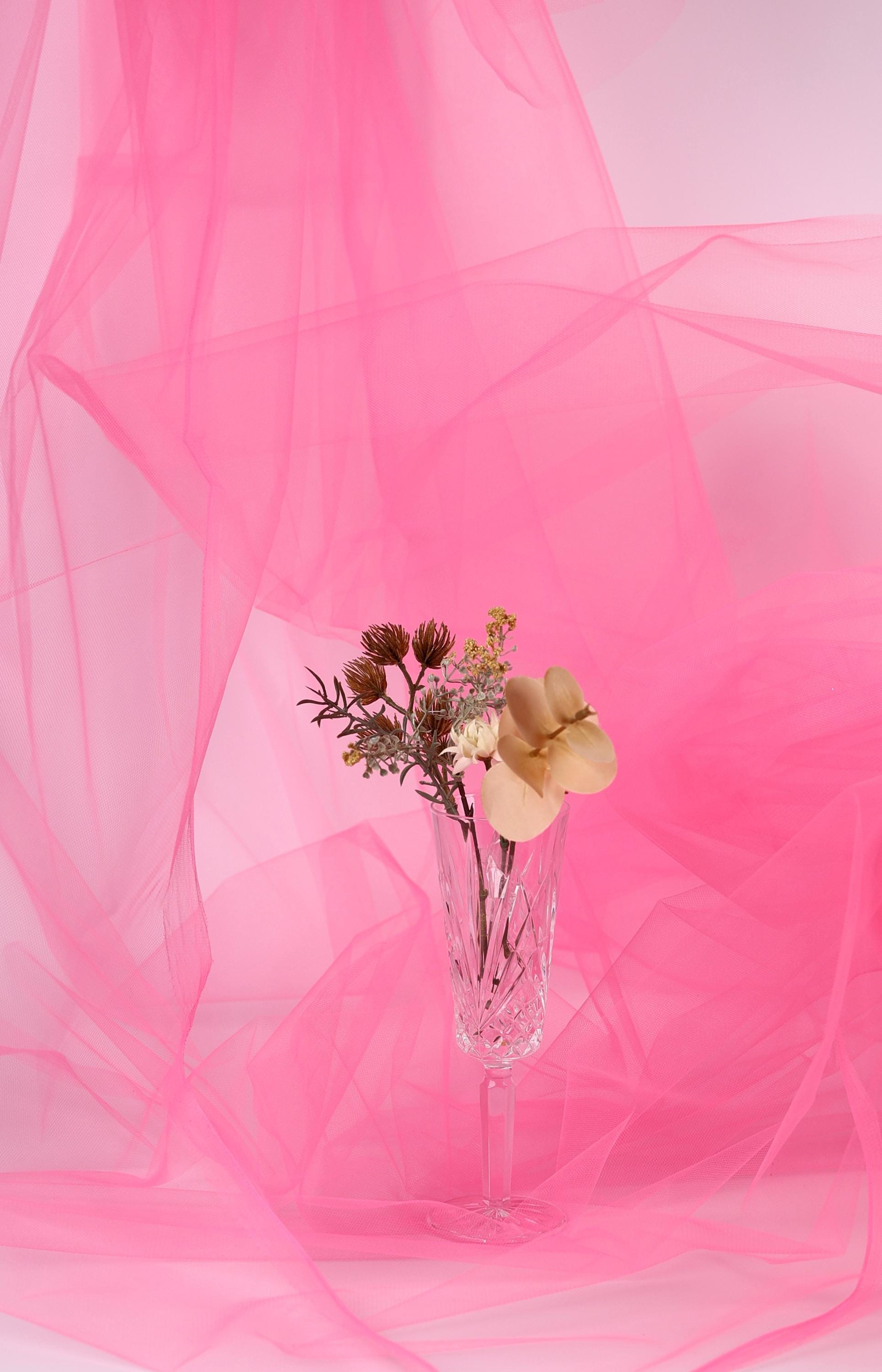 A clear glass vase filled with a bouquet of flowers sits on a pink background, creating a visually appealing and harmonious composition.