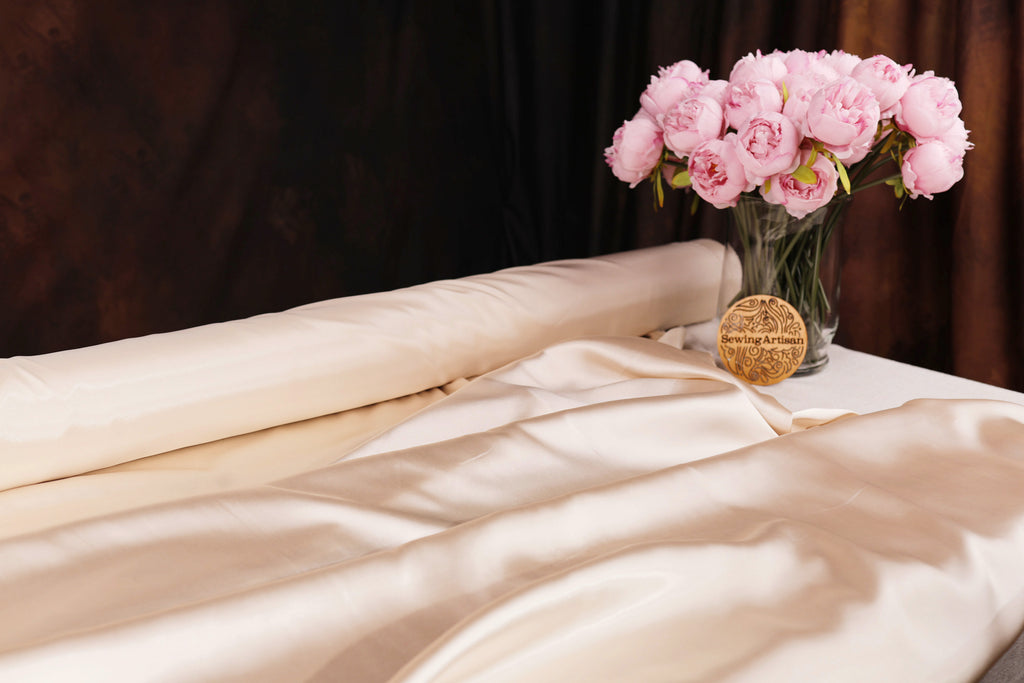 A bouquet of pink peonies in a glass vase sits on a white bedspread, with a gold medal placed next to it.