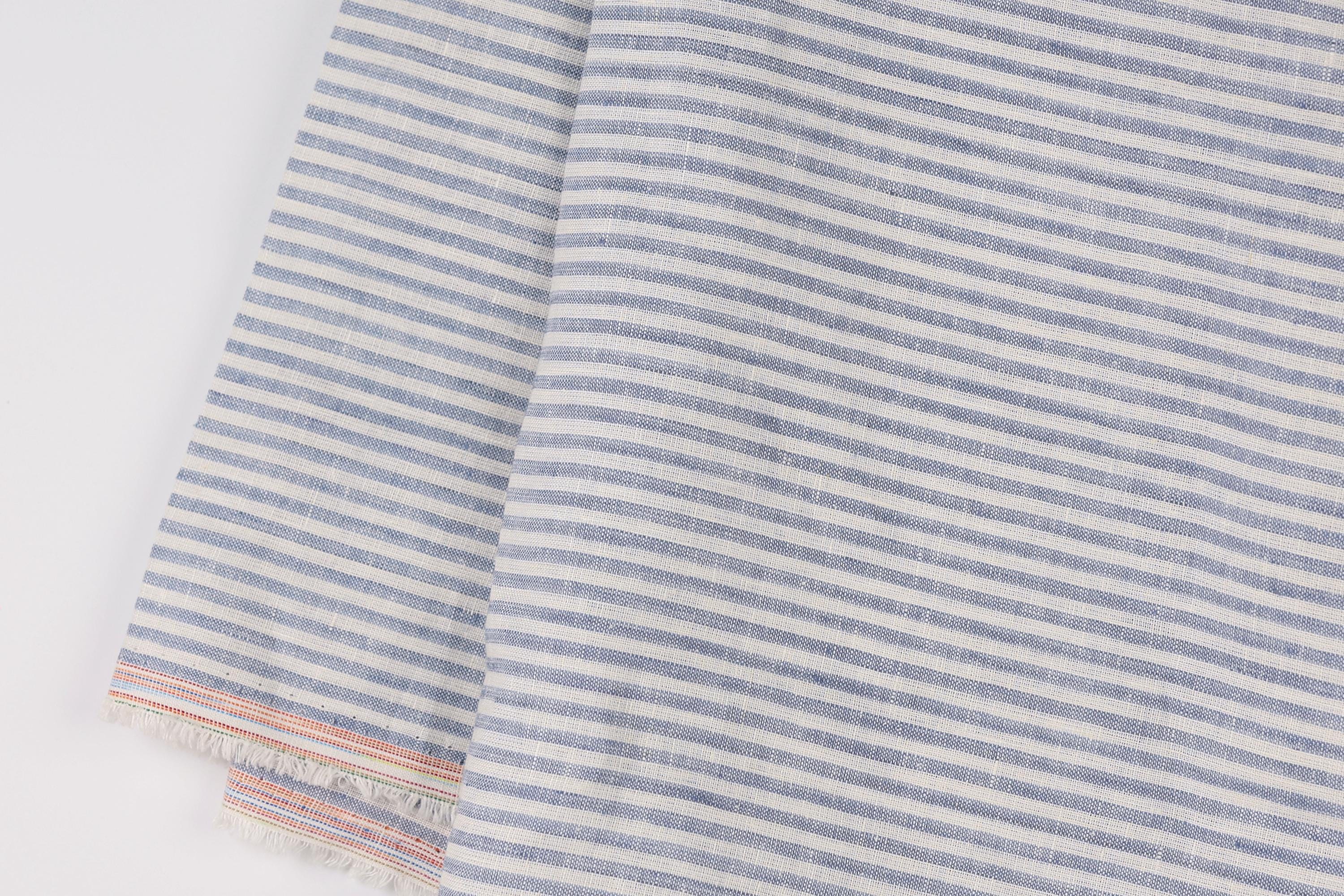 a close-up view of a fabric with a striped pattern in shades of blue and white. The fabric appears to be made of linen and has a textured appearance.