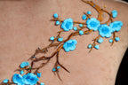a close-up view of a delicate embroidered design on a fabric, showcasing a branch with blue flowers and leaves.