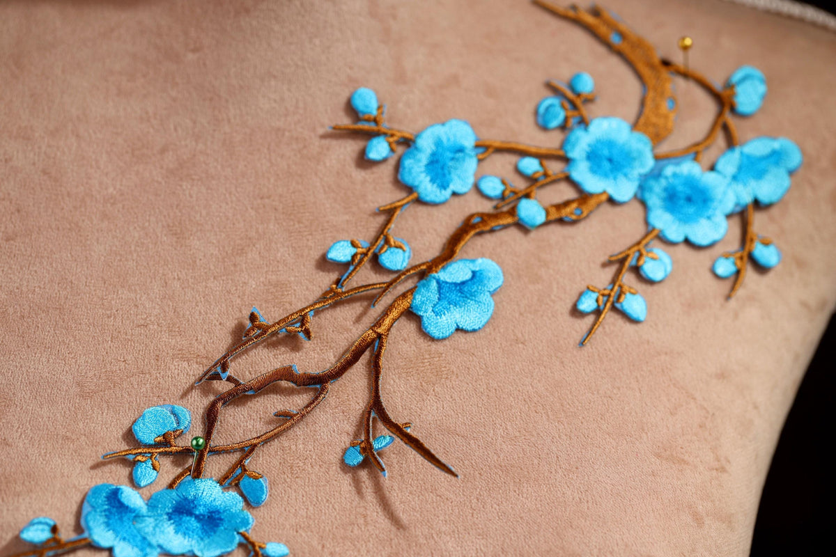 a close-up view of a delicate embroidered design on a fabric, showcasing a branch with blue flowers and leaves.