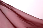 A close-up view of a flowing, maroon-colored fabric, possibly a sheer or sheer-like material, against a plain white background.