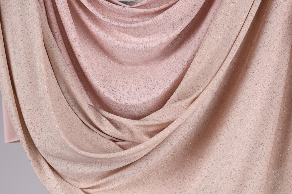 a close-up view of a fabric with a soft, flowing texture in shades of pink and beige. The fabric appears to be made of a shiny, glittery material, giving it a delicate and elegant appearance.