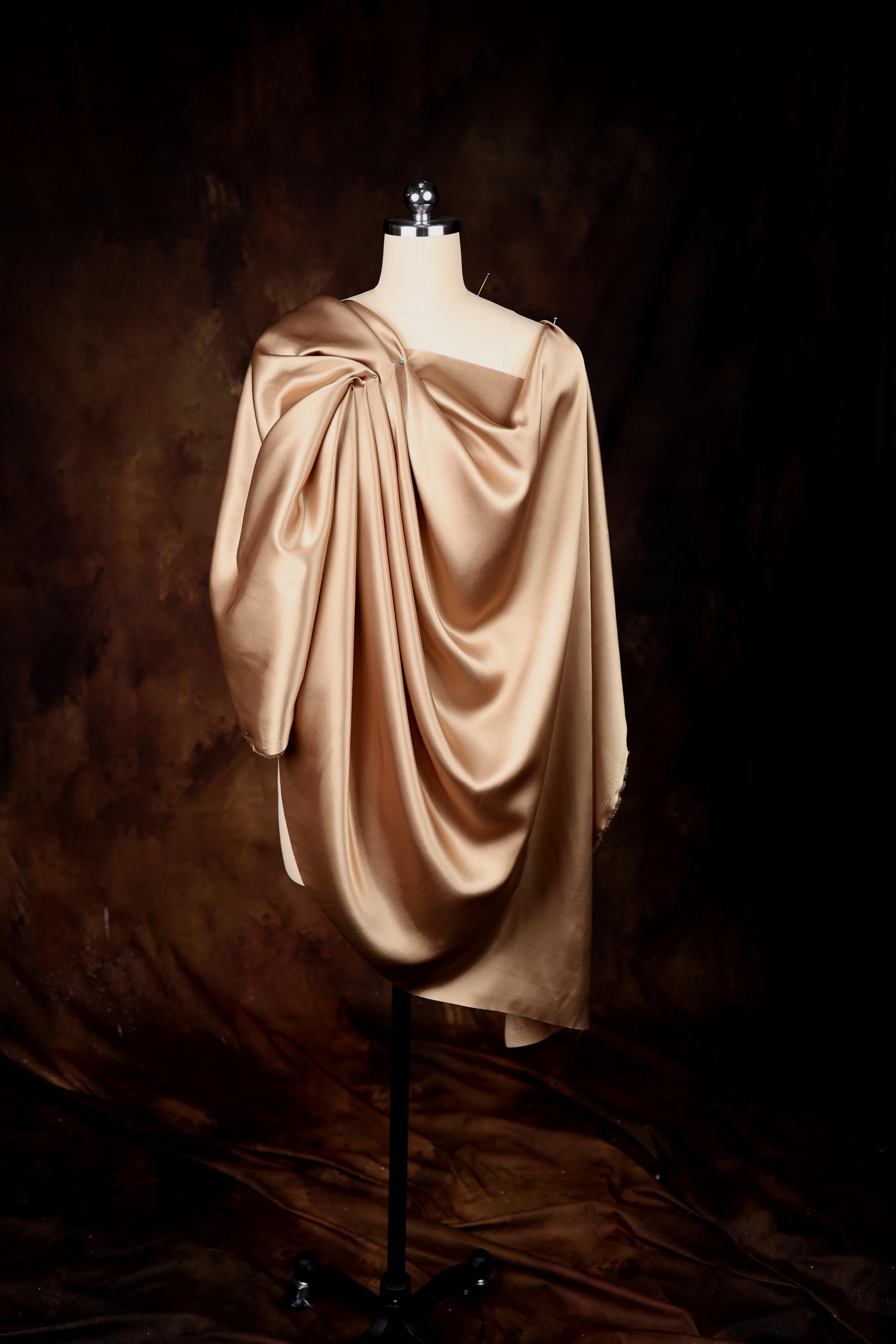 A gold-colored draped garment displayed on a mannequin against a dark background.