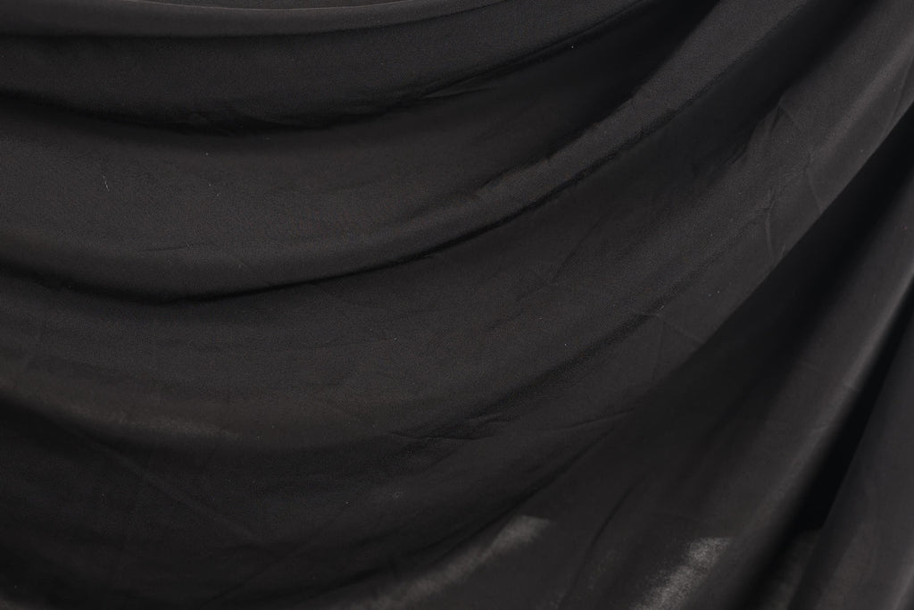 The image is a close-up of a black fabric, possibly a piece of clothing or a textile. The fabric appears to be wrinkled and has a textured surface, giving it a somewhat rough appearance.