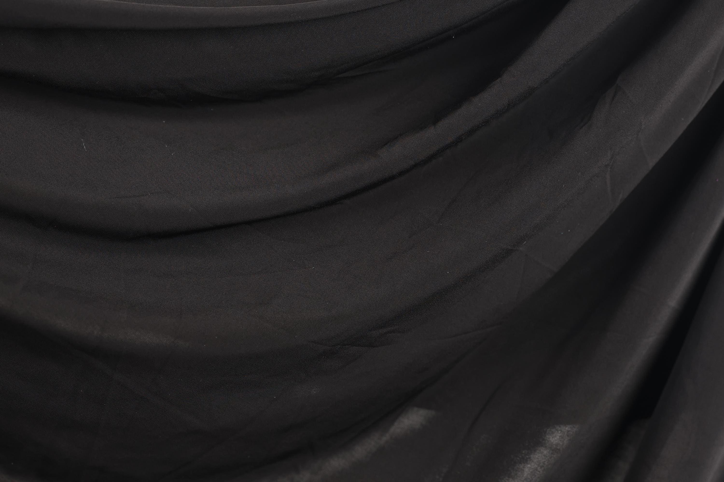 The image is a close-up of a black fabric, possibly a piece of clothing or a textile. The fabric appears to be wrinkled and has a textured surface, giving it a somewhat rough appearance.