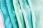 A close-up image of a collection of turquoise-colored satin fabric, with varying shades of turquoise visible.