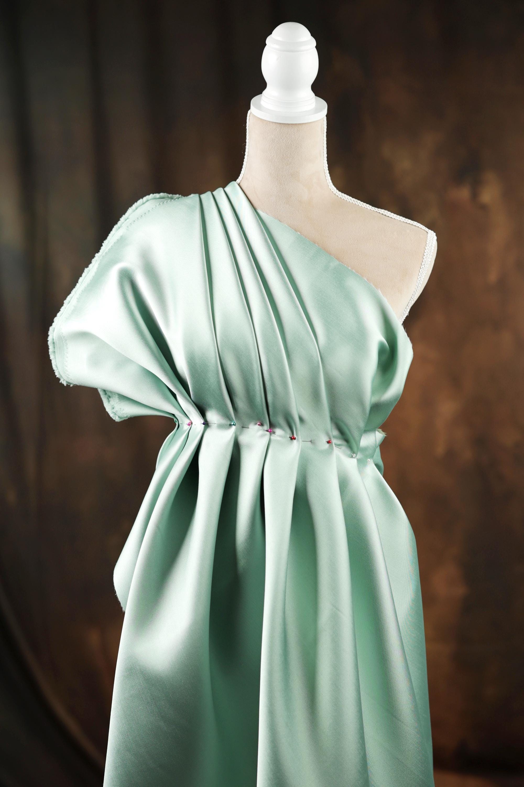 A mannequin wearing a green one-shoulder dress with a pleated design.