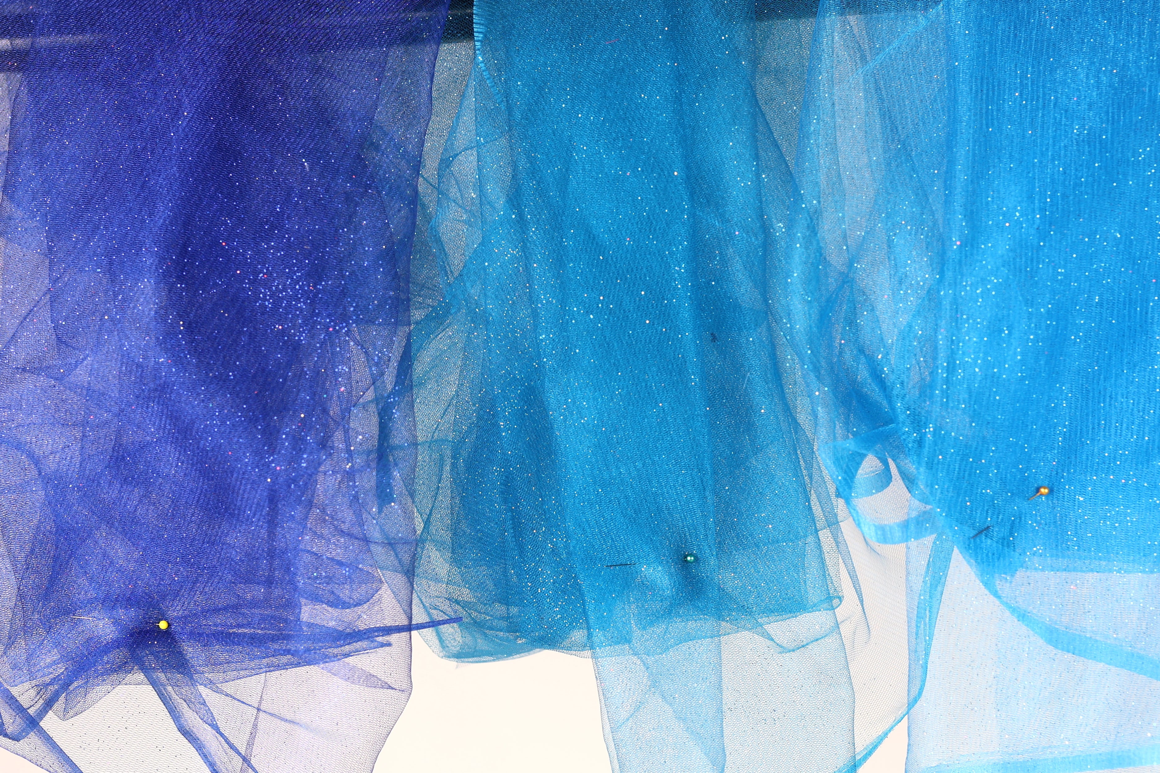 a close-up view of three blue fabric pieces with glittery textures, hanging together.