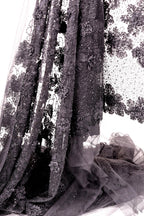 a close-up view of a delicate, intricately embroidered fabric with a floral pattern. The fabric appears to be made of sheer material, giving it a delicate and ethereal appearance. The image is a close-up of the fabric, showcasing its detailed embroidery and the intricate design elements.