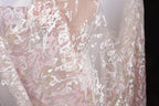 a close-up view of a delicate, lace-like fabric with a floral pattern in shades of pink and white. The fabric appears to be made of sheer material, giving it a soft and delicate appearance.