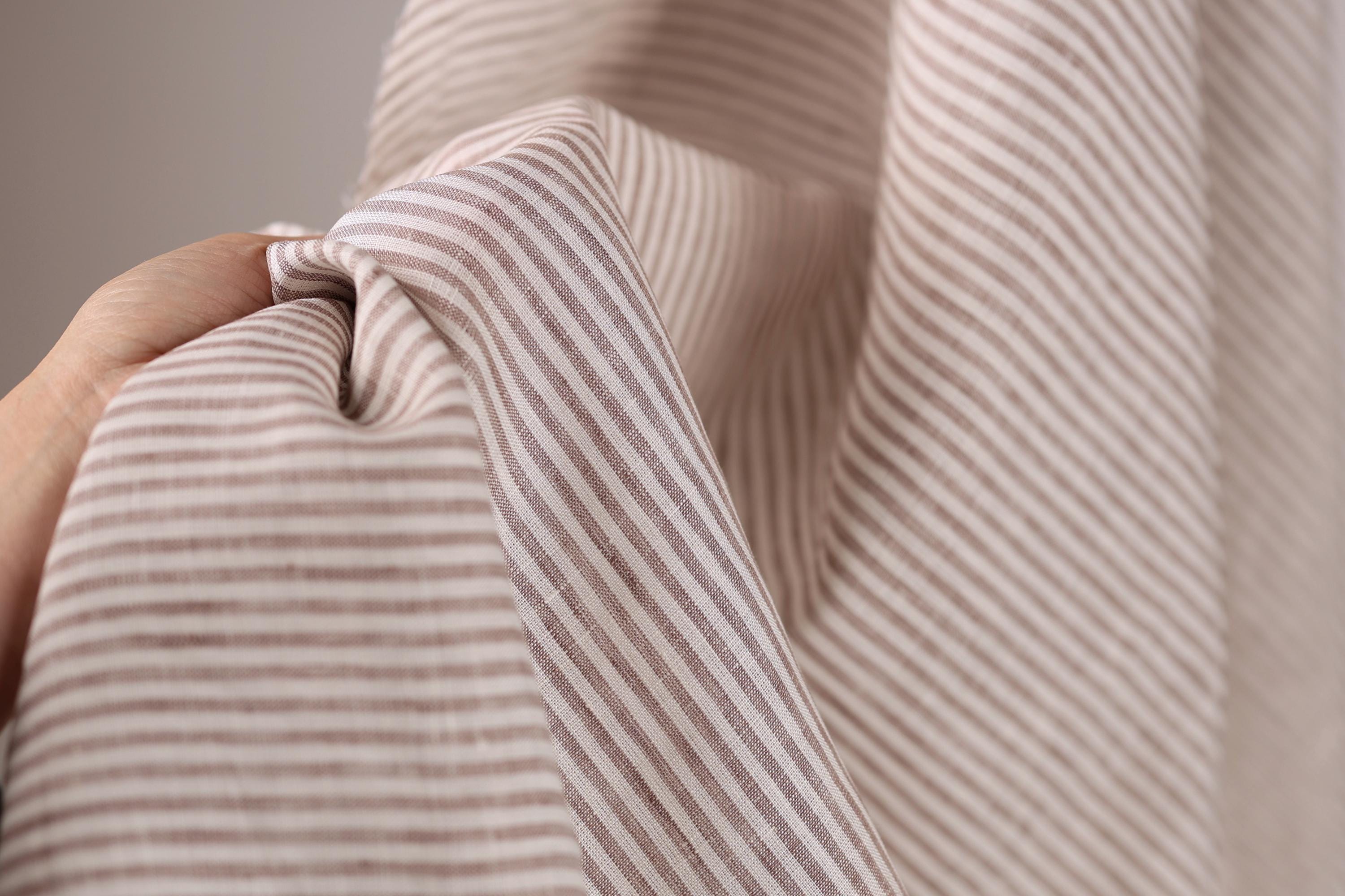 A hand is holding a piece of fabric with a striped pattern, which appears to be a light brown or beige color.