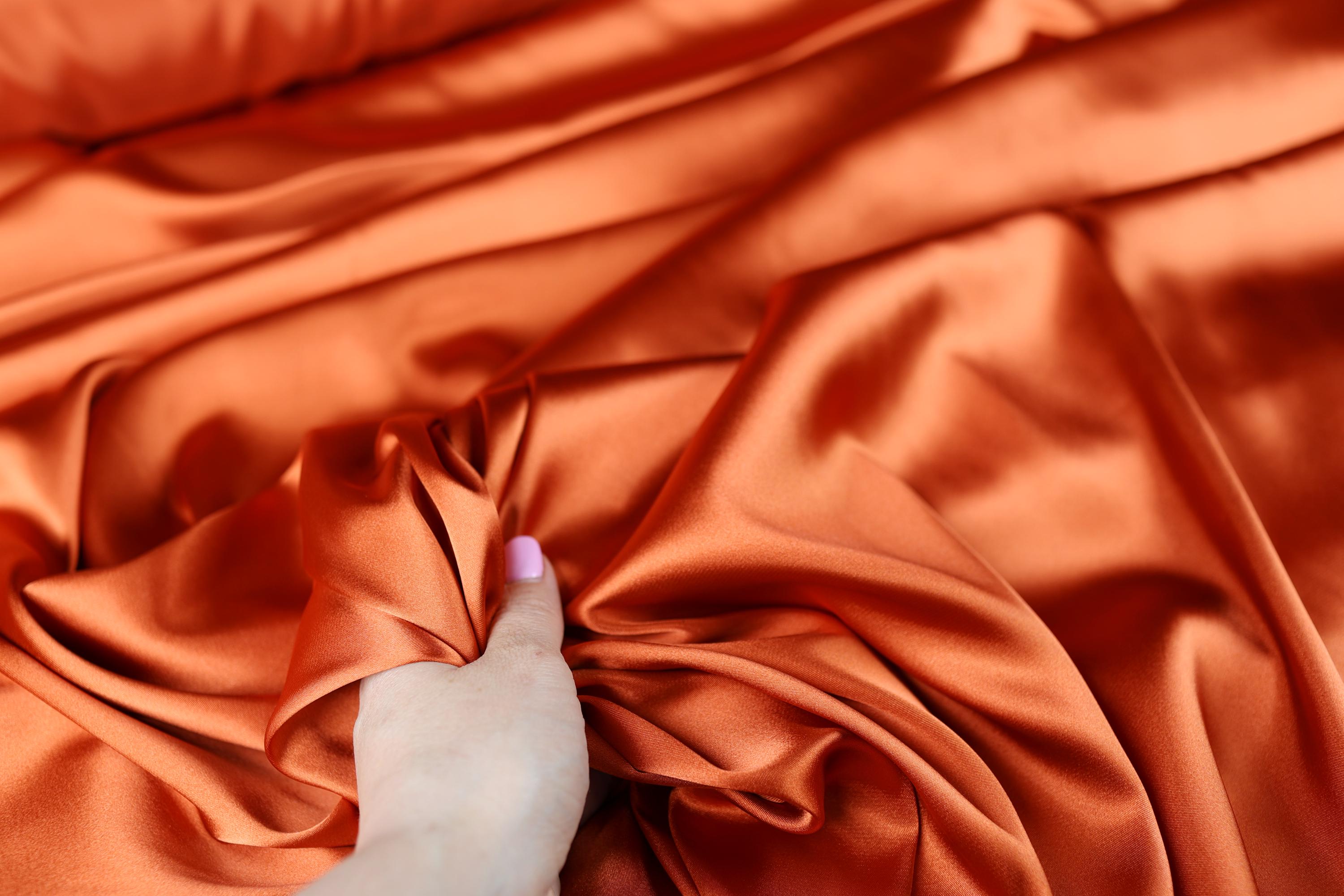 a person&#39;s hand on an orange satin fabric
