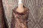 a mannequin wearing a brown sequin dress with a sheer overlay. The dress has a pattern of brown and black sequins, creating a visually striking and elegant design.