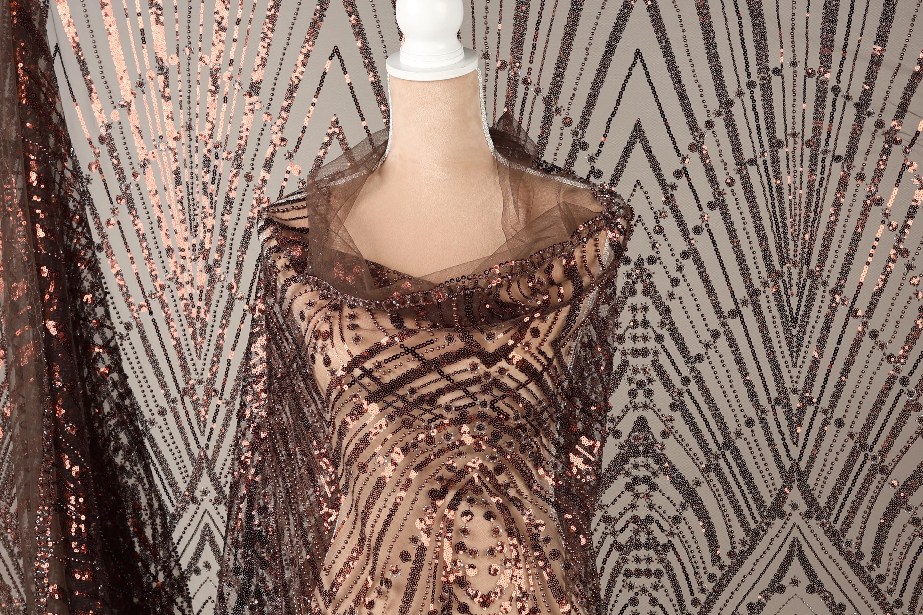 a mannequin wearing a brown sequin dress with a sheer overlay. The dress has a pattern of brown and black sequins, creating a visually striking and elegant design.
