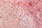 a close-up view of a delicate, pink fabric with a floral pattern. The fabric appears to be made of sheer material, with a lace-like texture and a shimmering, sequined effect. The pattern consists of small, repeating leaves and flowers, creating a delicate and intricate design. The fabric is the main focus of the image, with no other objects or text present.