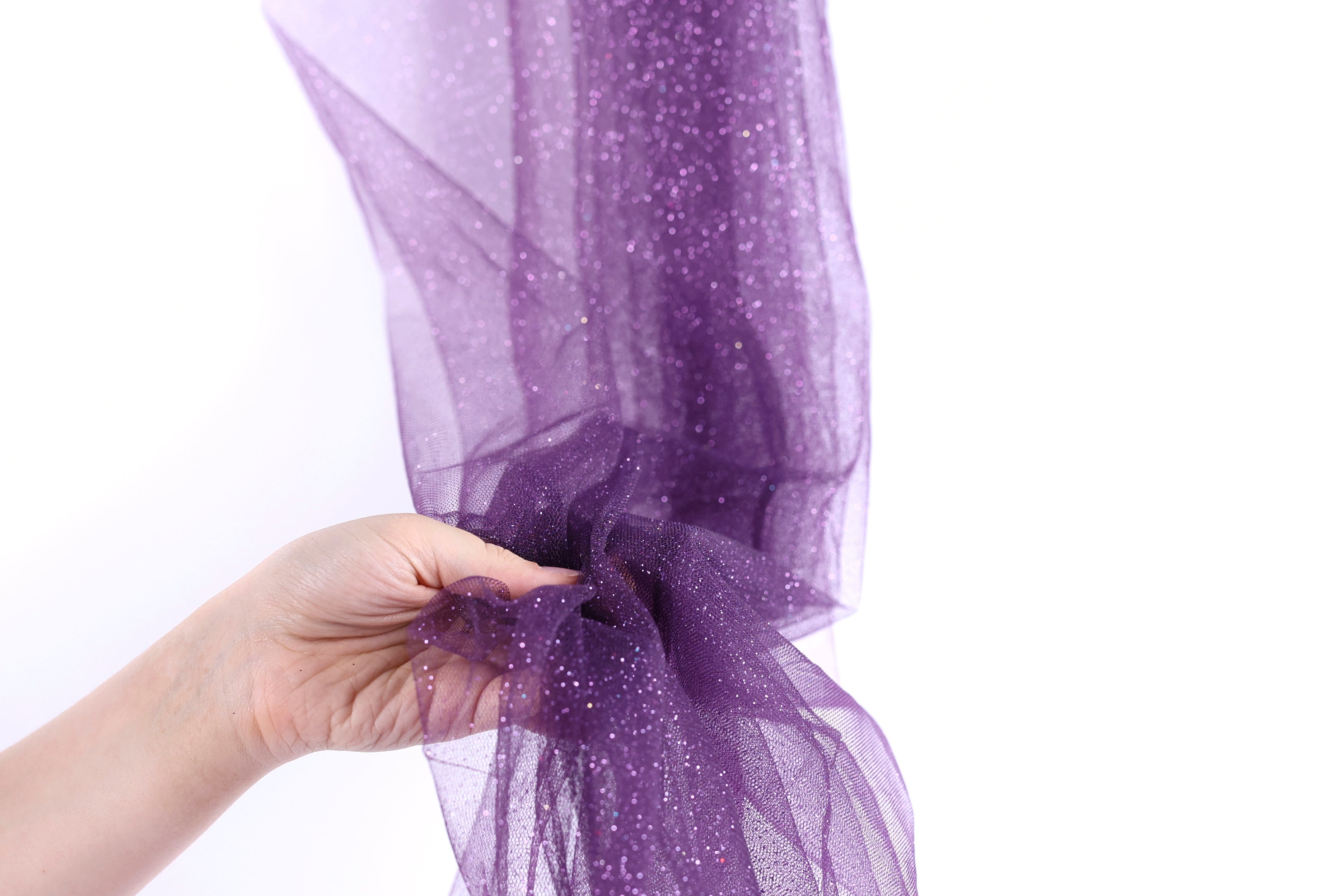 A hand is holding a piece of purple glittery fabric, which appears to be a sheer or sheer-like material.