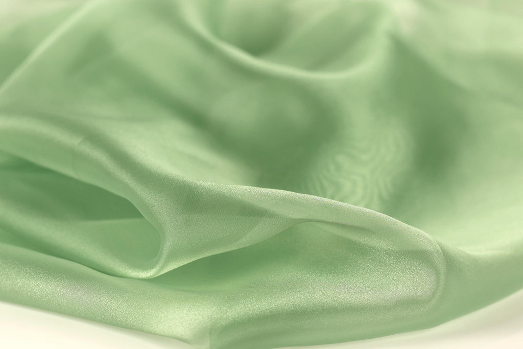 A close-up view of a soft, flowing green fabric, possibly silk or chiffon, with a smooth and shiny texture.
