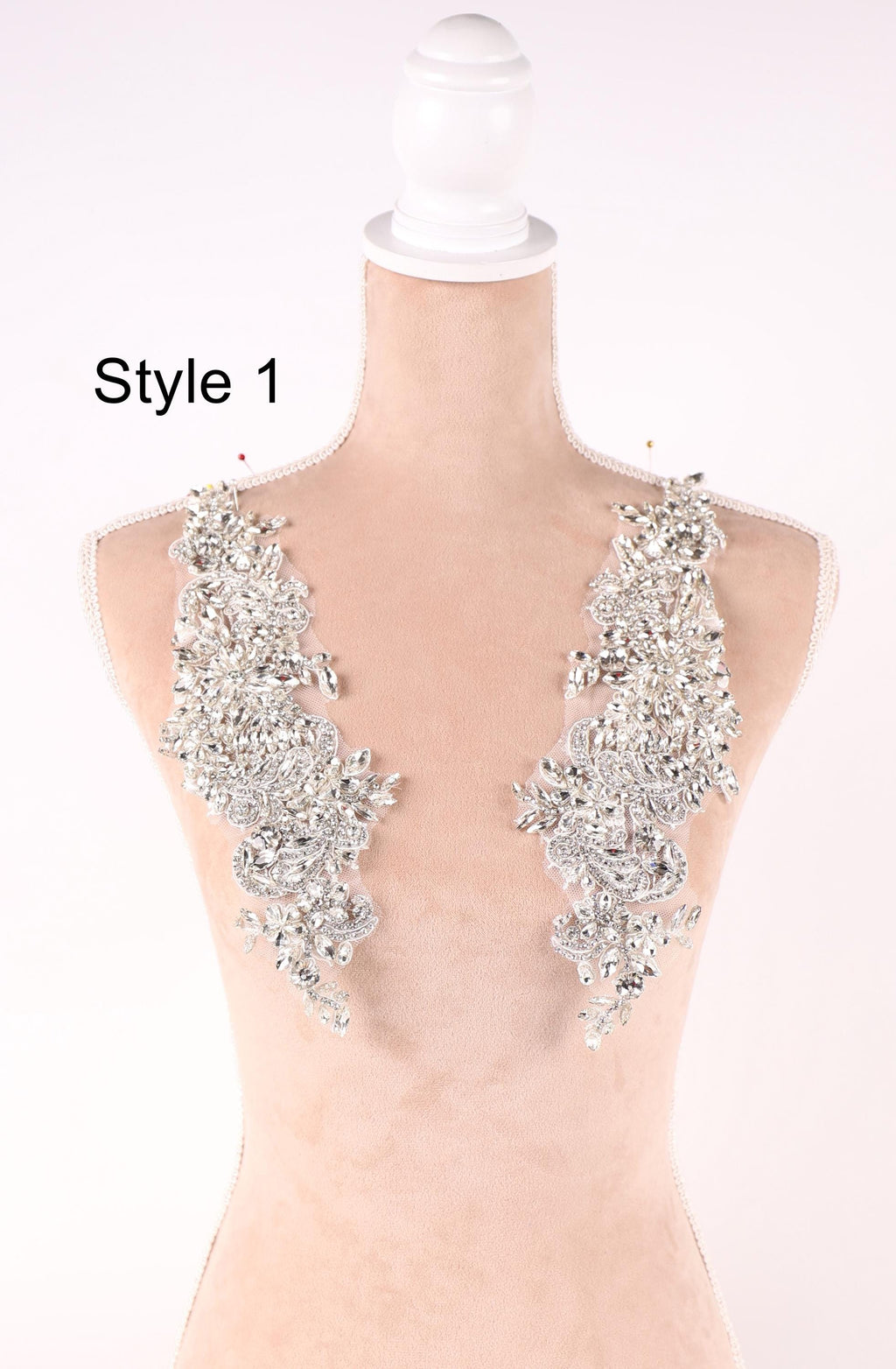 A mannequin with a white head and a beige body, wearing two large, sparkling silver embellishments on its shoulders.