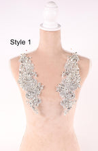 A mannequin with a white head and a beige body, wearing two large, sparkling silver embellishments on its shoulders.