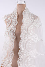A mannequin wearing a white lace shawl with intricate floral embroidery.