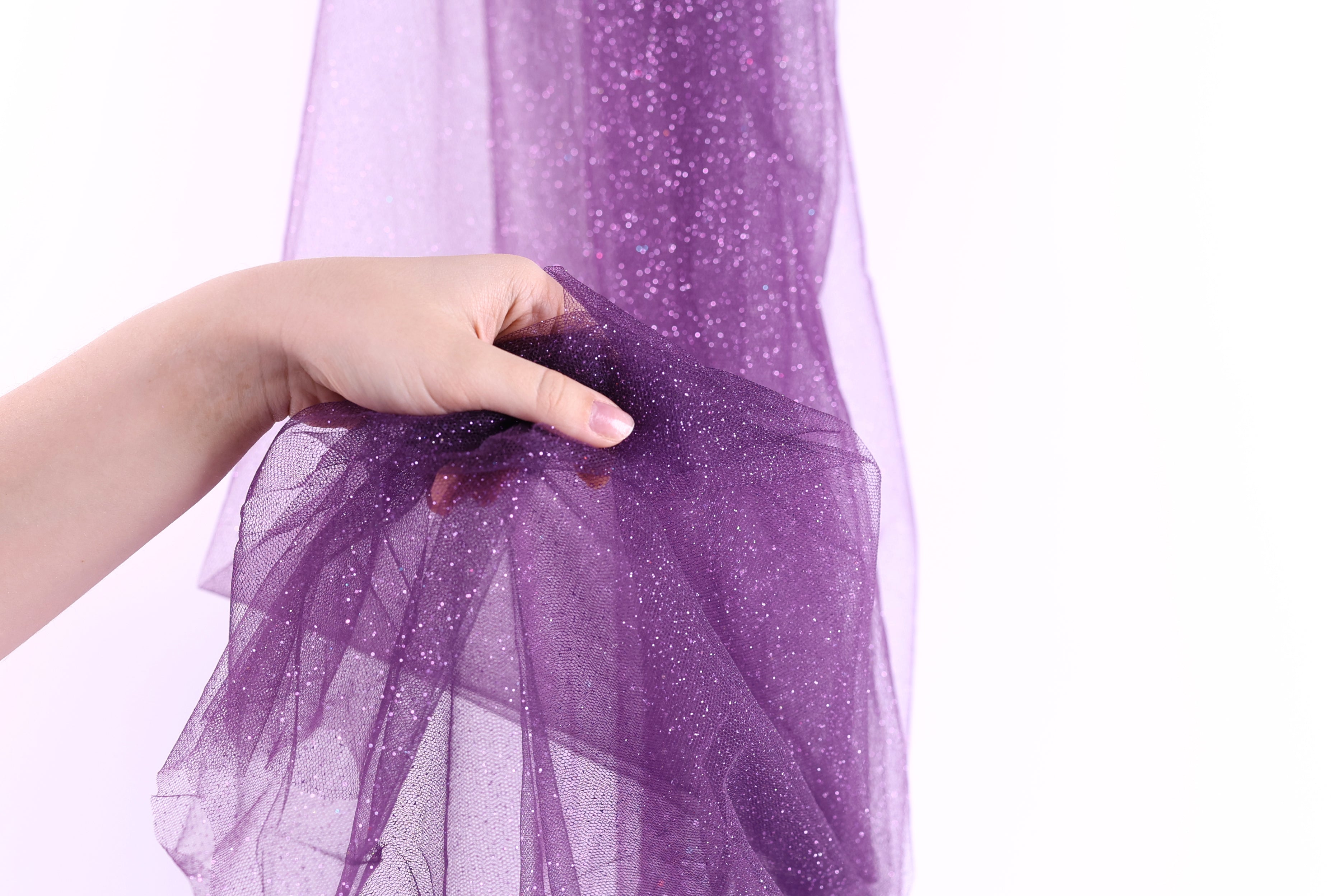 A hand is holding a piece of purple glittery fabric, which appears to be a sheer or sheer-like material.