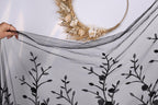 a hand holding a black fabric with a floral pattern, including leaves and flowers, against a white background.