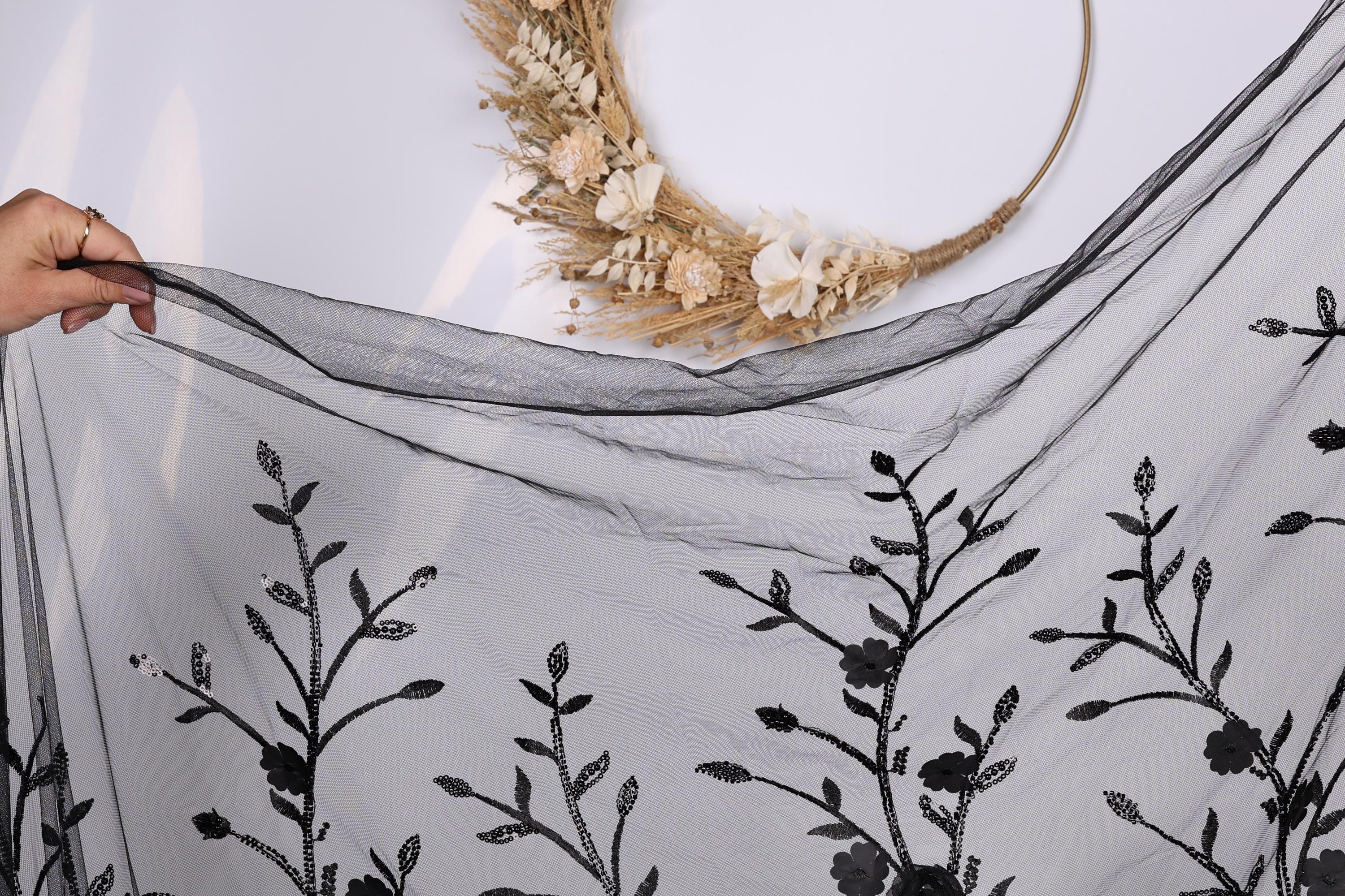 a hand holding a black fabric with a floral pattern, including leaves and flowers, against a white background.